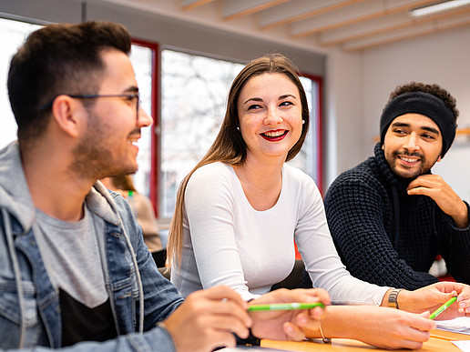 Three students are sitting at a table, chatting and laughing.