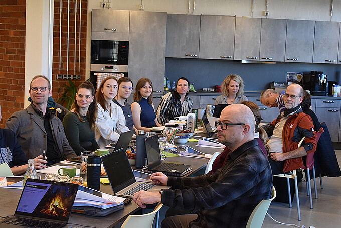 The workshop participants sit at a full table and listen to the presentation.