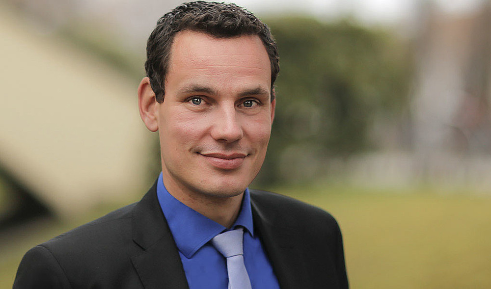 Professor Erik Hahn wears a suit with a blue shirt and absorbent cotton and smiles into the camera.