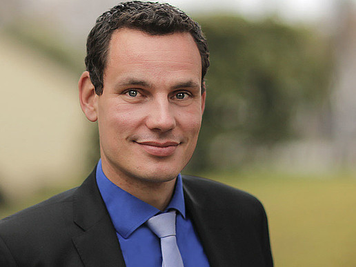 Professor Erik Hahn wears a suit with a blue shirt and absorbent cotton and smiles into the camera.