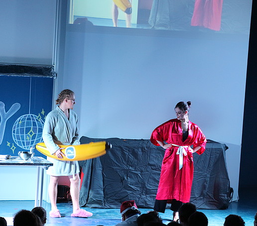 A woman in a red bathrobe and a man with an inflatable banana are on stage.