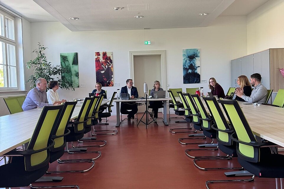 Members of the Personnel Development Commission sit at conference tables in the Senate Hall of the HSZG and discuss matters. The Rector sits at the front.