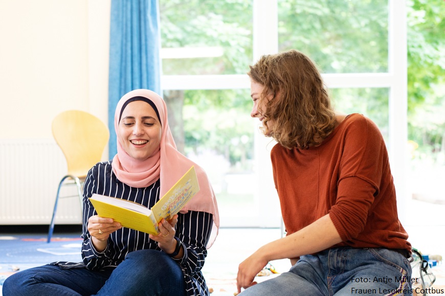 Two women are sitting on the floor laughing.