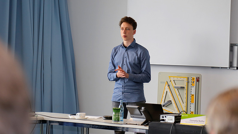 German scholarship holder Lucas Wünsche during a voluntary assignment for the StuRa. He stands in front of an audience in the seminar room and gives a speech.