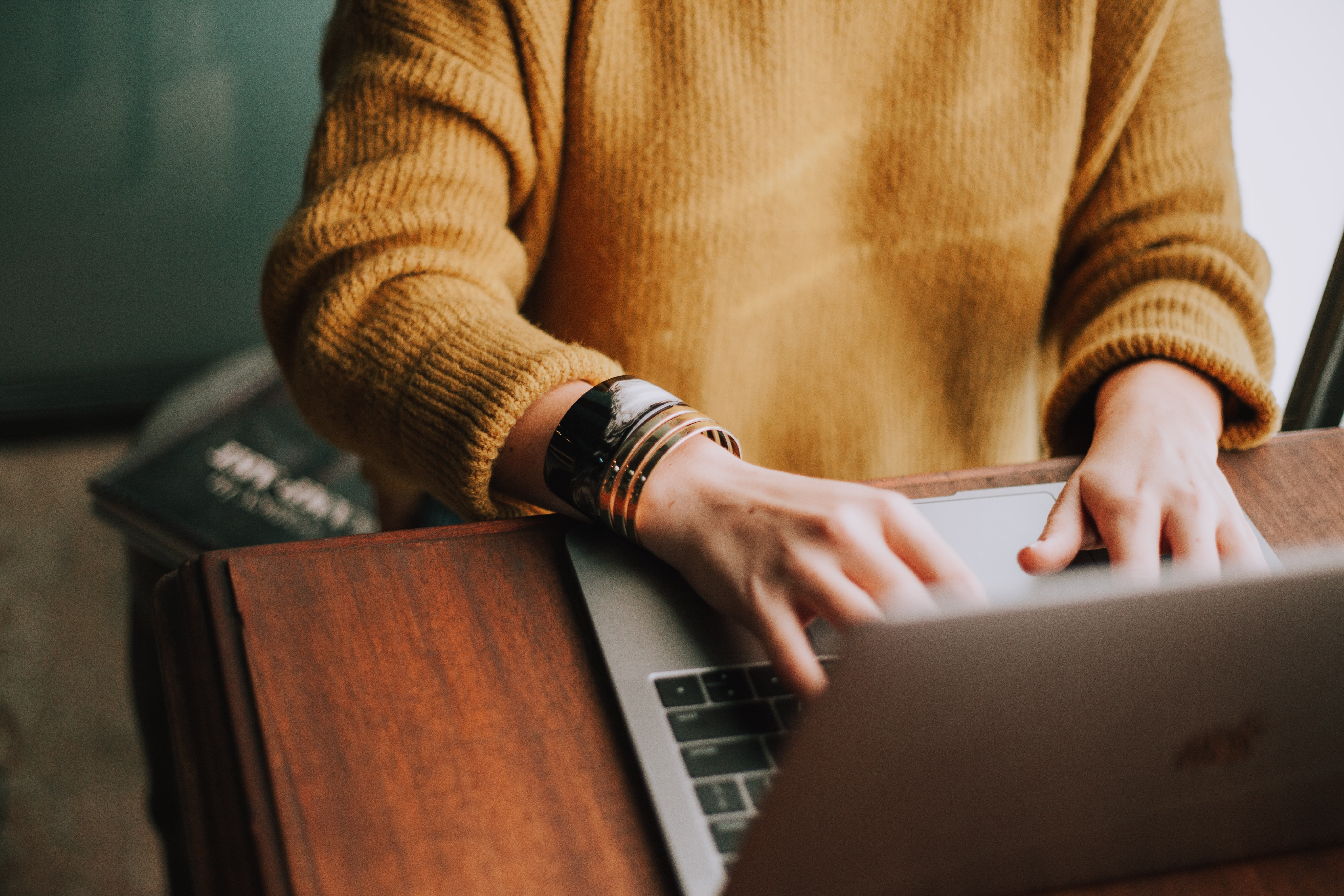 A person is sitting at a laptop. All you can see is her yellow sweater and her hands writing on the keyboard.